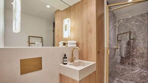 A modern bathroom with a wooden vanity, a sink with a gold faucet, and a marble shower area. - Studio Louvre Museum Palais-royal (Paris)