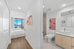 A modern hotel room with a balcony, a large window, a bed, a bathroom with a toilet and sink, and artwork on the walls.