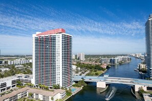 A high-rise hotel with multiple floors, a river in the foreground, and a bridge connecting two areas.