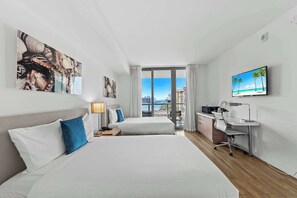 A hotel room with two beds, a desk, a TV, and a view of the city.