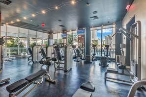A gym with various exercise equipment, large windows, and a view of the city. - Waterfront Pool • Beach Service • 7th Floor (Hallandale Beach)