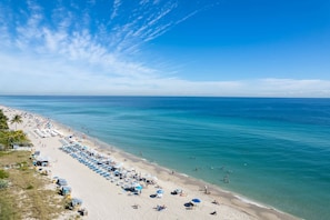 A beach with rows of sun loungers and umbrellas, a clear sky, and calm sea.