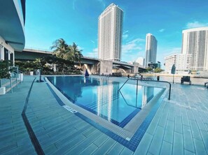 A swimming pool with a 3ft 9in depth marker, surrounded by a tiled deck and palm trees, with tall buildings in the background.