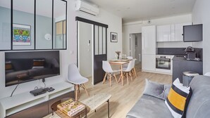Ein modernes Wohnzimmer mit Flachbildfernseher, einem grauen Sofa und einem Essbereich mit Holztisch und Stühlen.