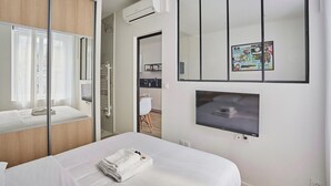 Ein modernes Hotelzimmer mit einem Bett, einem Fernseher, einem Spiegel und einer Schiebetür zu einem Badezimmer.