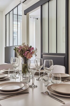 Una mesa de comedor dispuesta con platos, vasos y cubiertos, con un jarrón de flores en el centro.