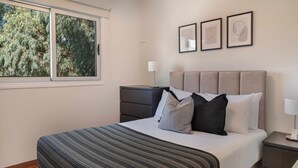 A neatly arranged bedroom with a bed, bedside tables, a lamp, and framed artwork on the wall. - Phaedrus Living Evergreen City Flat (Strovolos)