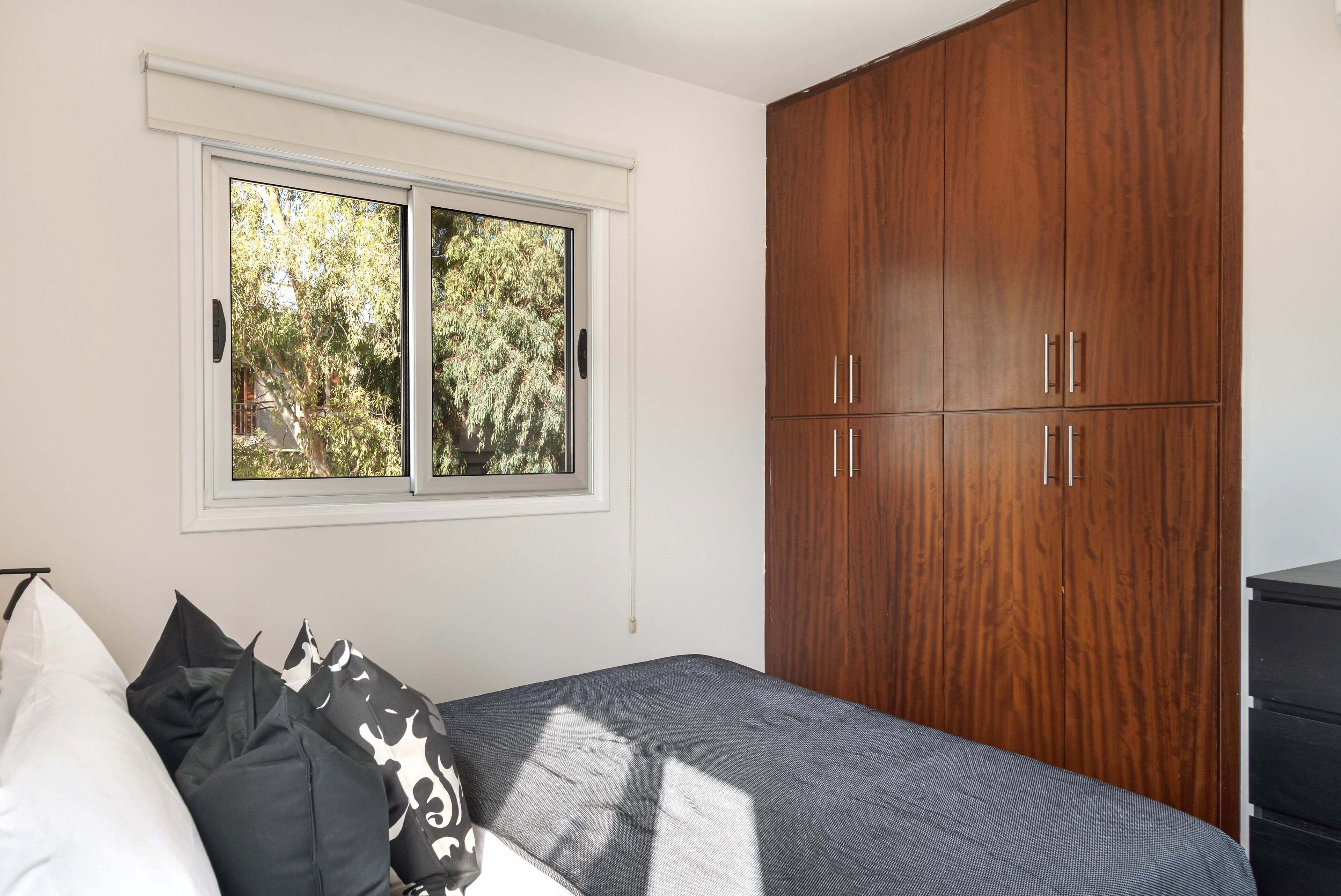 A bedroom with a bed, a window, and a wooden wardrobe.