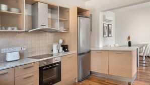 A modern kitchen with a built-in oven, a stainless steel refrigerator, and wooden cabinets. - Phaedrus Living Evergreen City Flat (Strovolos)