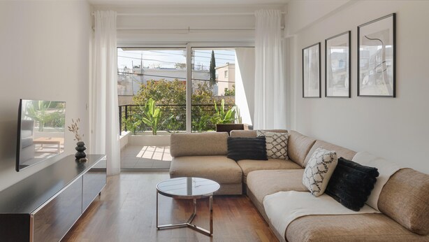 A modern living room with a sofa, a coffee table, and a TV on a stand. There are three framed pictures on the wall and a balcony with plants. - Phaedrus Living Evergreen City Flat (Strovolos)