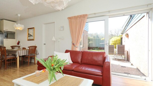 Una sala de estar con un sofá rojo, una mesa de centro blanca y un comedor con sillas y una mesa de madera.