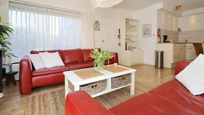 Una sala moderna con un sofá rojo, una mesa de centro blanca y un área de cocina al fondo.