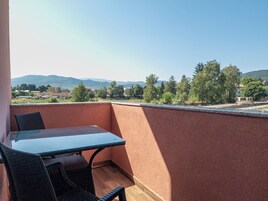 Un balcón con mesa y sillas, con vistas a un paisaje pintoresco con árboles y colinas al fondo.
