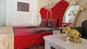 A bedroom with a red tufted headboard, patterned bedding, a mirror with a gold frame, and a small elephant figurine on a table.
