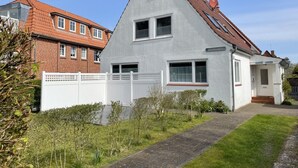 A two-story house with a sloped roof, a white fence, and a paved driveway. - Ferienwohnung in St. Peter-ording (St. Peter-Ording)