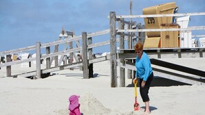 A beach scene with a wooden boardwalk, a lifeguard tower, and a sandy area with a child and an adult. - Ferienwohnung in St. Peter-ording (St. Peter-Ording)