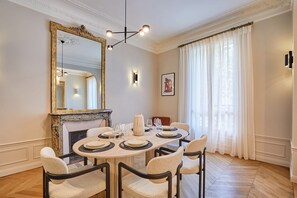 A dining room with a marble table, four upholstered chairs, a large ornate mirror, a fireplace, and a chandelier. - Amazing Apartment Saint Germain des Pres With A-C (Paris)