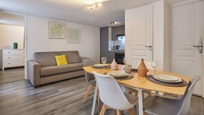 Un salon moderne avec un coin repas, comprenant un canapé, une table à manger, des chaises et une cuisine en arrière-plan.