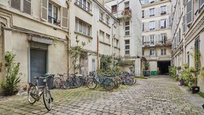 Une cour intérieure où sont garés des vélos le long des murs, un chemin pavé et des bâtiments dotés de balcons et de fenêtres.