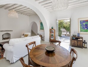 Cozy living space with a central table, sofa, and staircase leading to an upper level, offering a view of the outdoors.