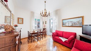 Un salon avec un canapé rouge, une table à manger en bois, un lustre et un tableau accroché au mur.
