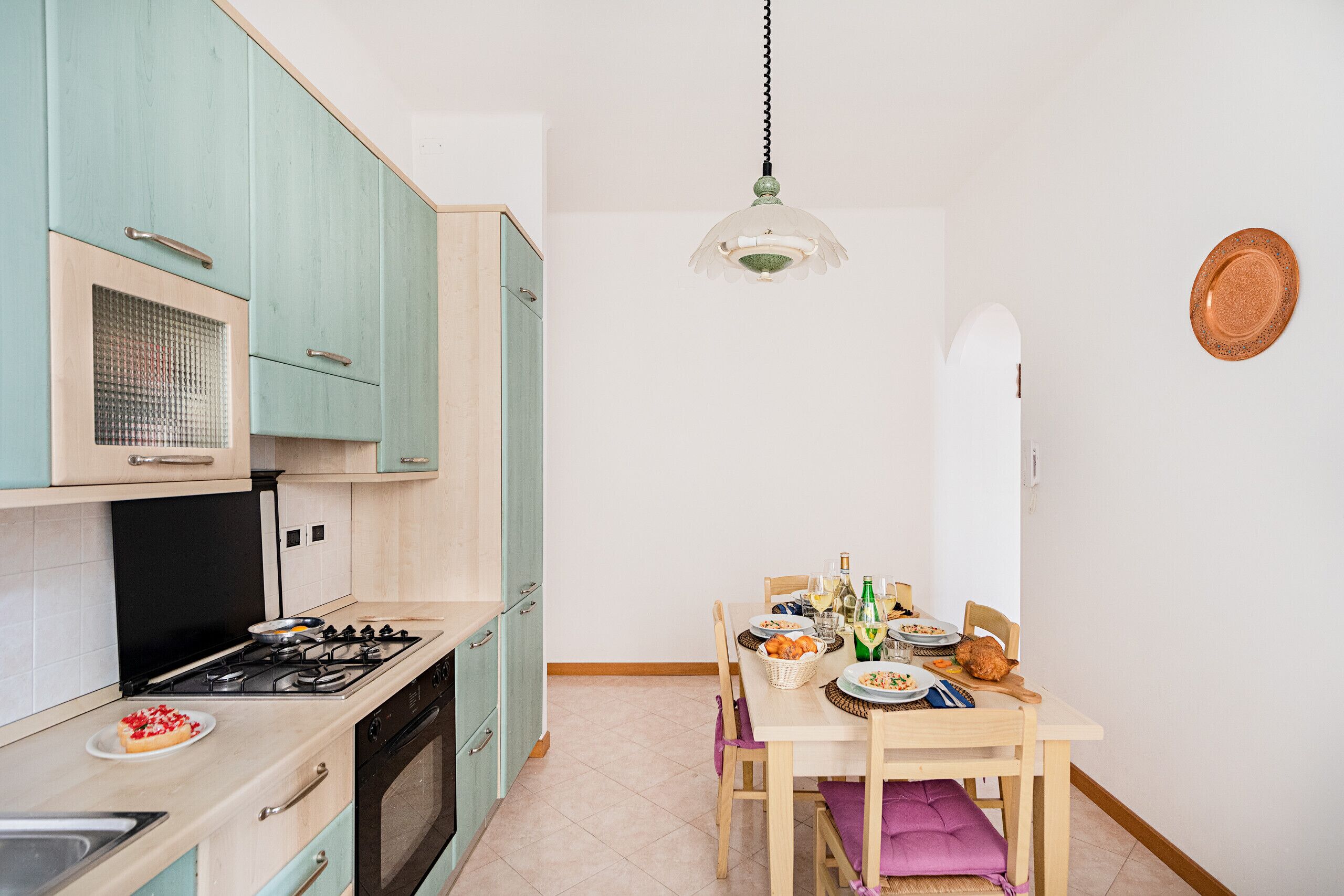 A kitchen with teal cabinets, a stove, and a dining table set with plates and bottles.