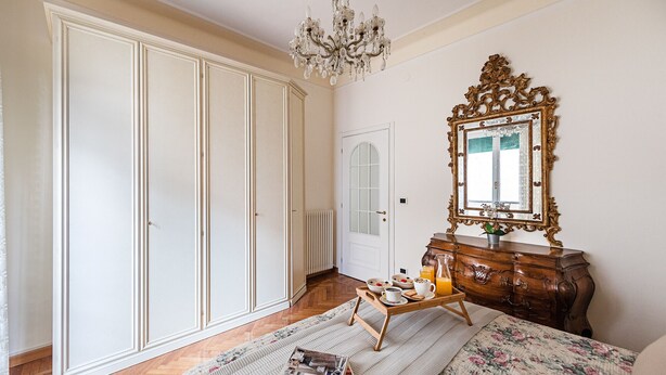 Une chambre dotée d’une grande armoire, d’une commode avec un miroir, d’un plateau pour le petit-déjeuner et d’un lit recouvert d’une couvre-lit à motifs floraux.