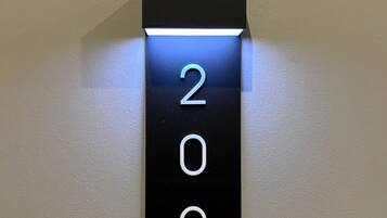 A black, illuminated number plate with the digits 209 on a plain wall.