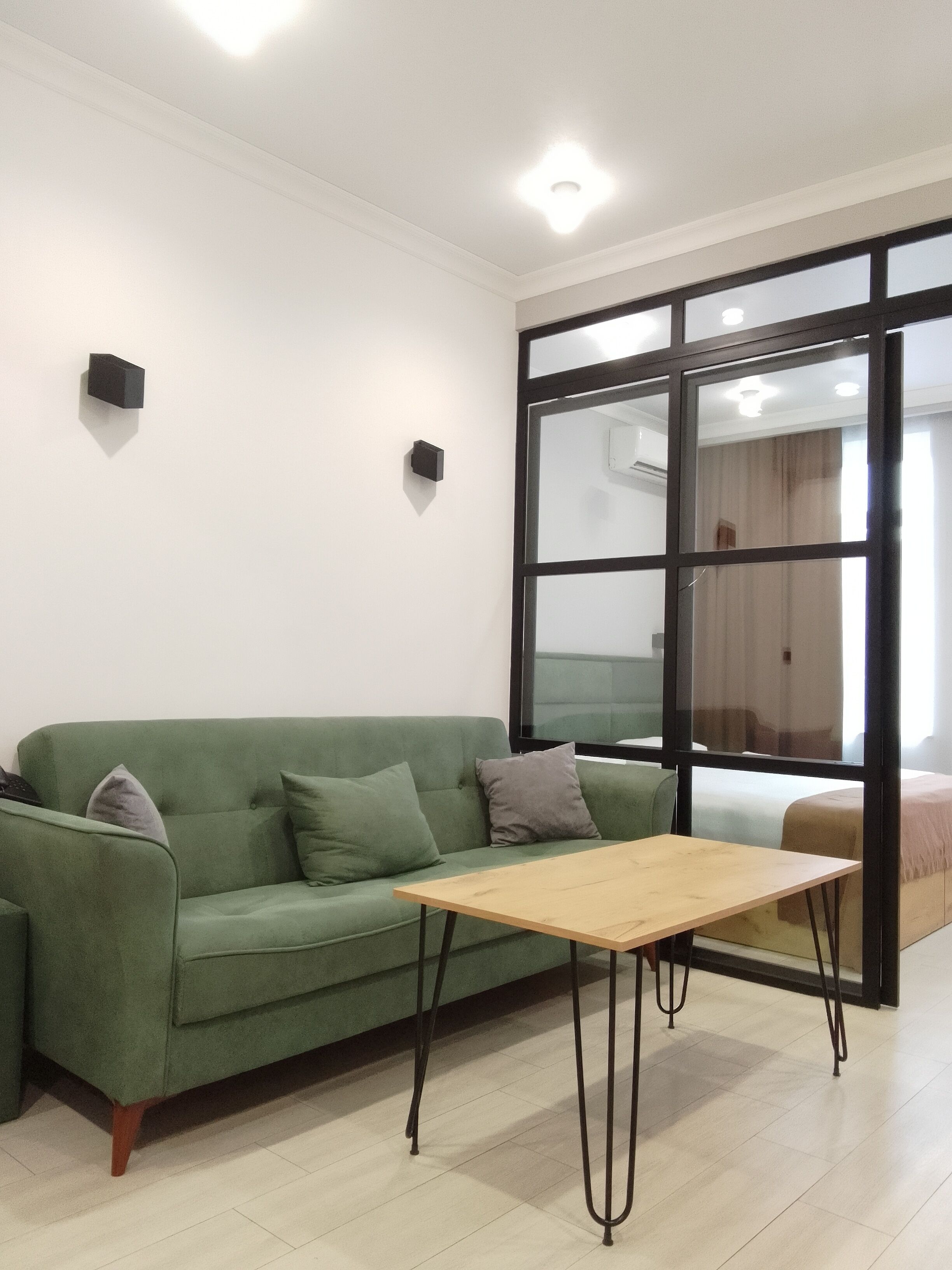 Un sofá verde con cojines, una mesa de madera y un ventanal con vistas.