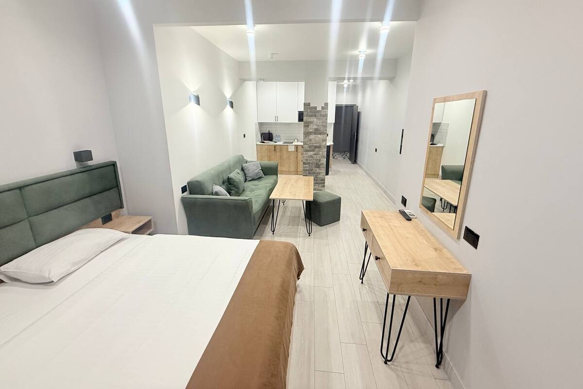 A modern hotel room with a bed, a sofa, a small table, and a mirror.