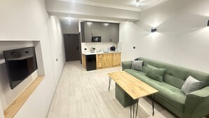 A modern kitchen with a microwave, sink, and wooden cabinets. There is a green sofa with cushions and a wooden coffee table. - NineRooms Apart-Hotel (Yerevan)