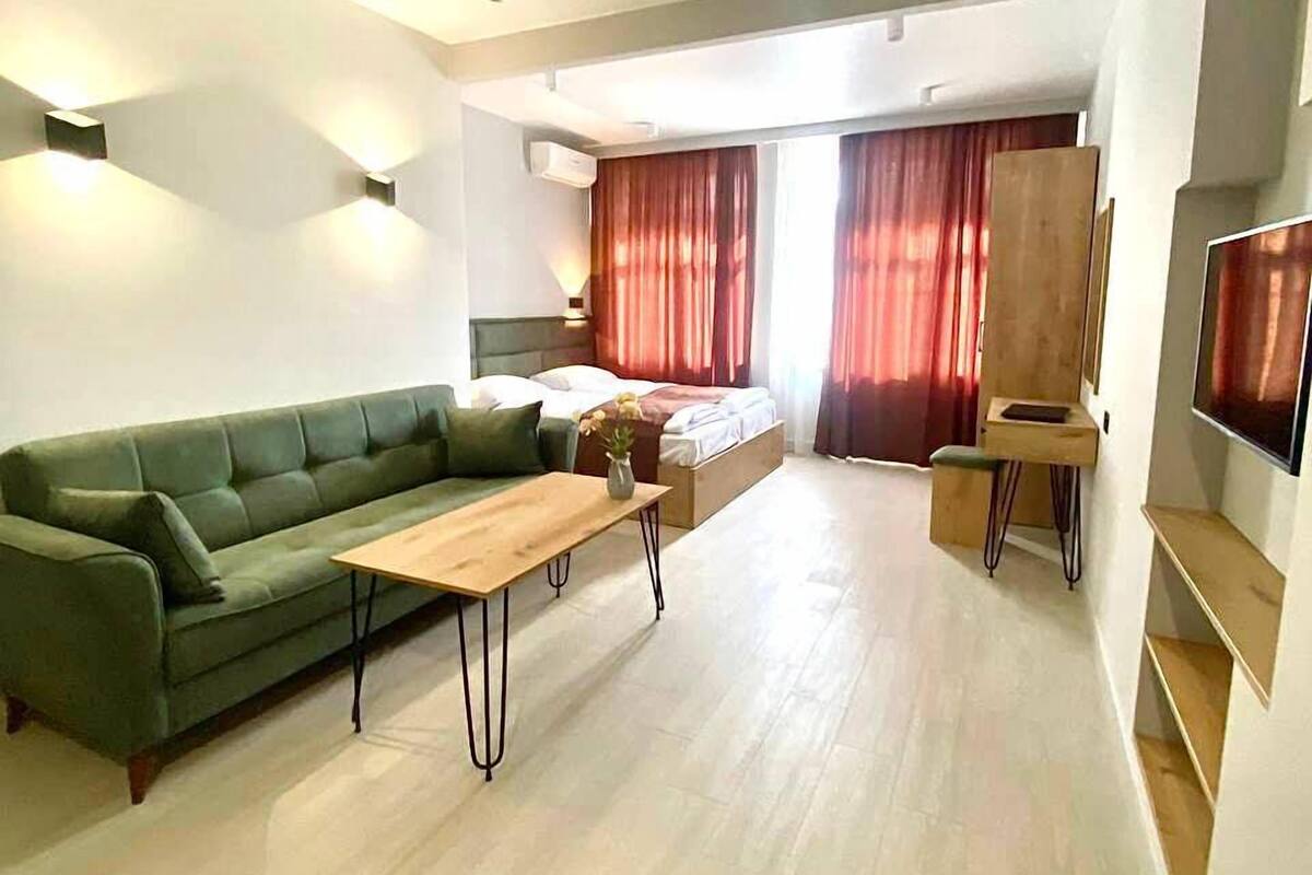 A modern living room with a green sofa, a wooden coffee table, and a painting on the wall.