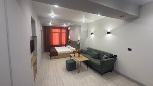 A modern hotel room with a bed, a green sofa, a small table, and a TV. - NineRooms Apart-Hotel (Yerevan)