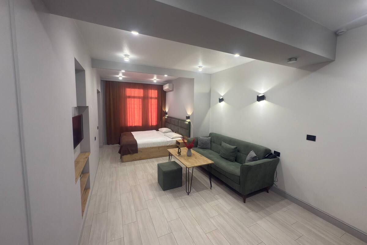 A modern hotel room with a bed, a green sofa, a small table, and a TV.