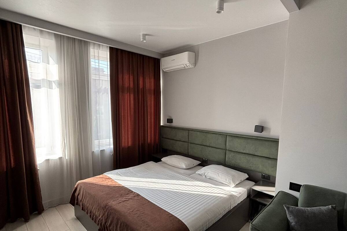 A modern hotel room with a large bed, a green upholstered armchair, and a window with curtains.