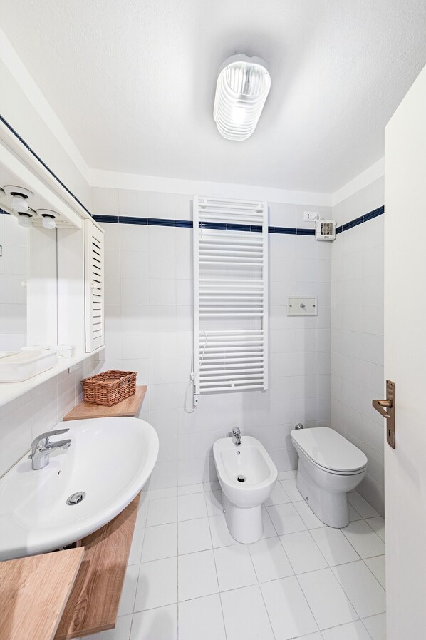 Ein modernes Badezimmer mit weißem Waschbecken, Bidet und WC, einem Holz-Waschtisch und einem Handtuchhalter.