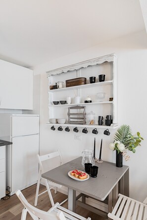 Eine Küche mit weißen Schränken, einem Esstisch mit Stühlen und einem an der Wand befestigten Regal mit verschiedenen Küchenutensilien.