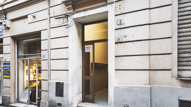 Um edifício com portas numeradas, entrada visível e acesso direto pela rua com uma placa.