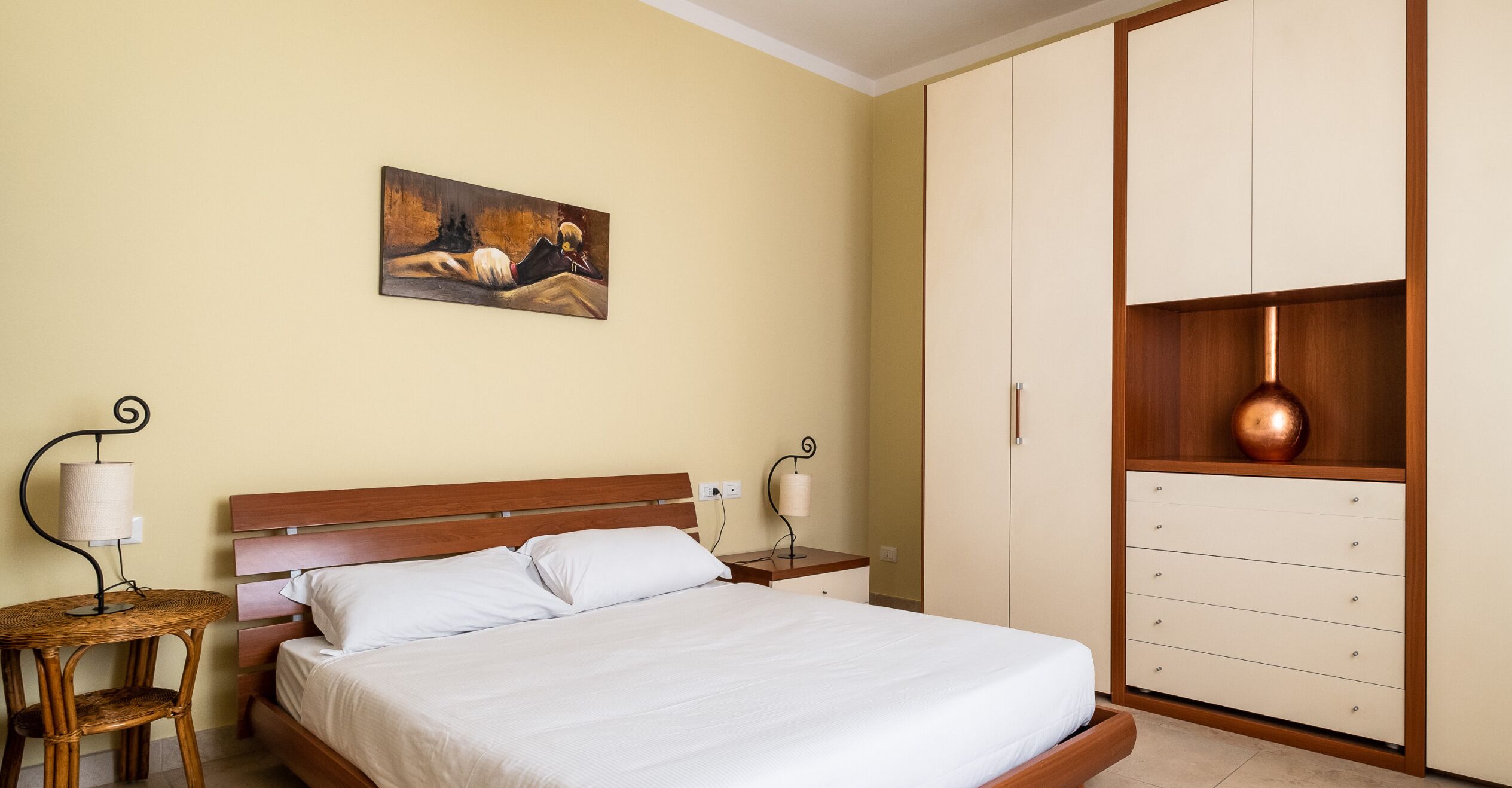 Una camera da letto con un letto, comodini, una lampada, un quadro e un armadio.