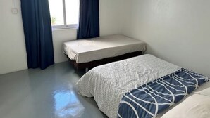 A small, single-room accommodation with a bed, a window with curtains, and a plain floor.