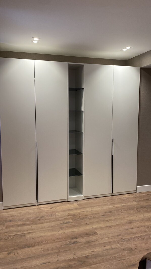 A room with a wooden floor, a built-in wardrobe with multiple compartments, and recessed ceiling lighting.