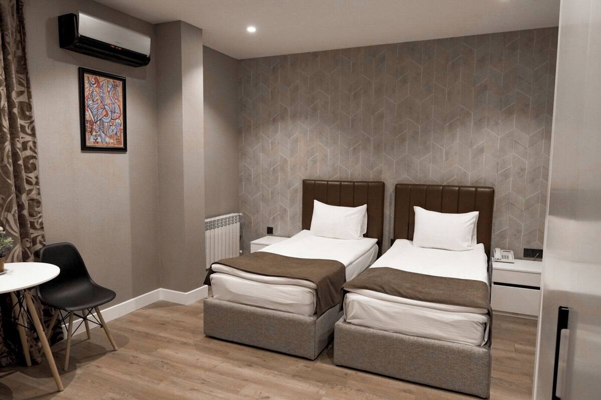 Ein Hotelzimmer mit zwei Betten, einem kleinen Tisch, einem Stuhl und einer Heizung.
