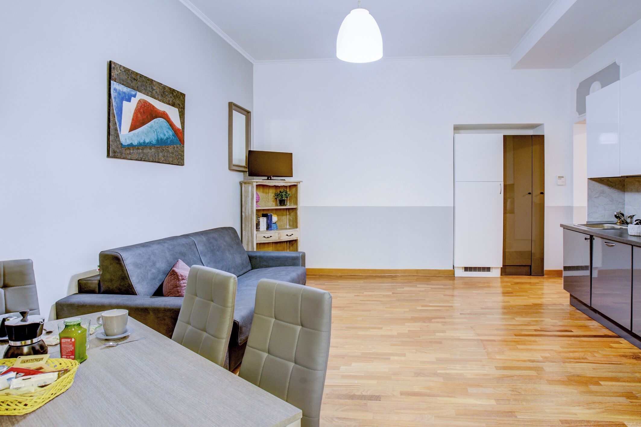 A modern living room with a grey sofa, a dining table with chairs, a coffee table, and a painting on the wall.