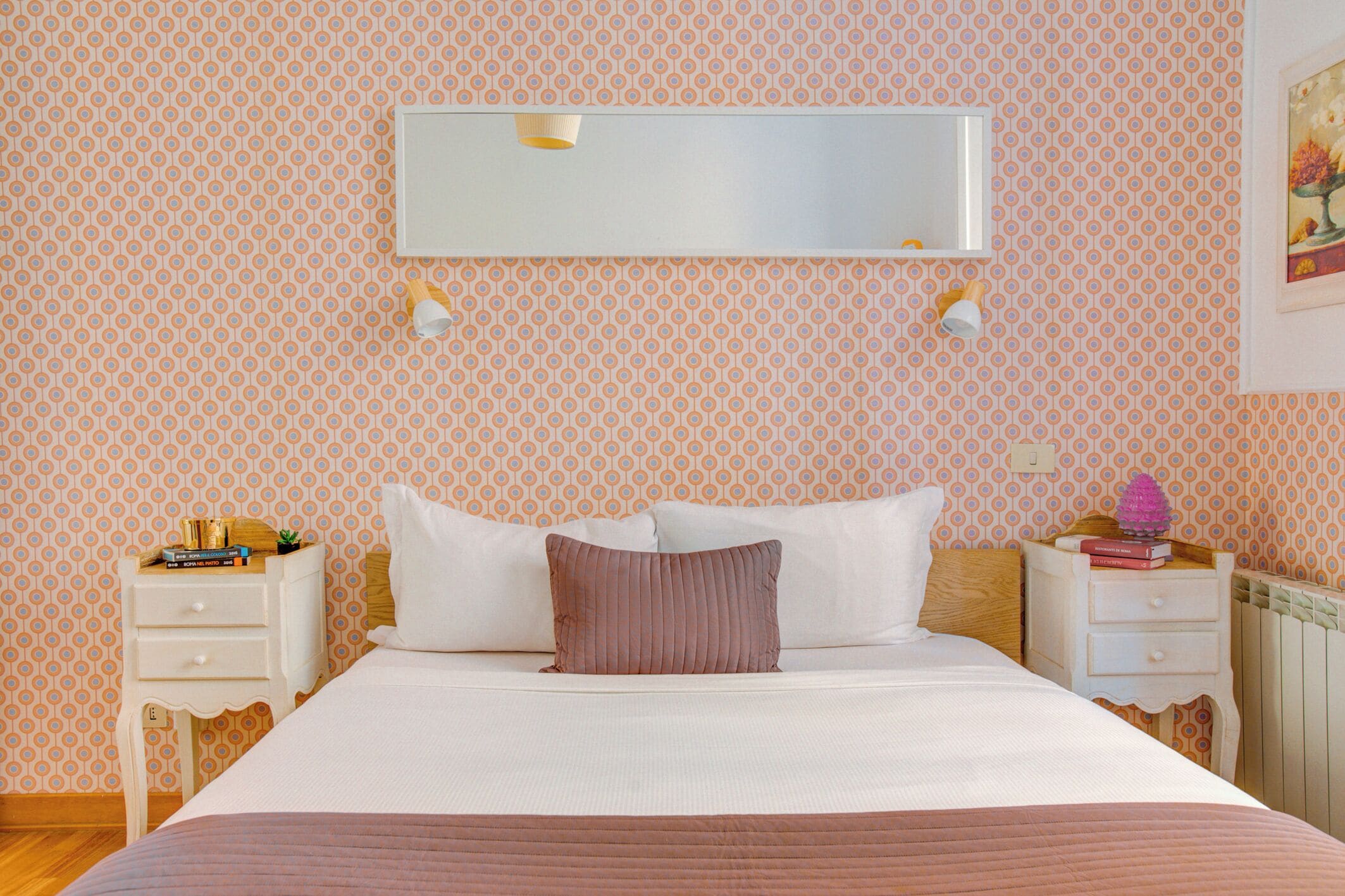 A neatly made bed with a white and brown bedspread, two bedside tables with lamps, and a wall-mounted mirror.