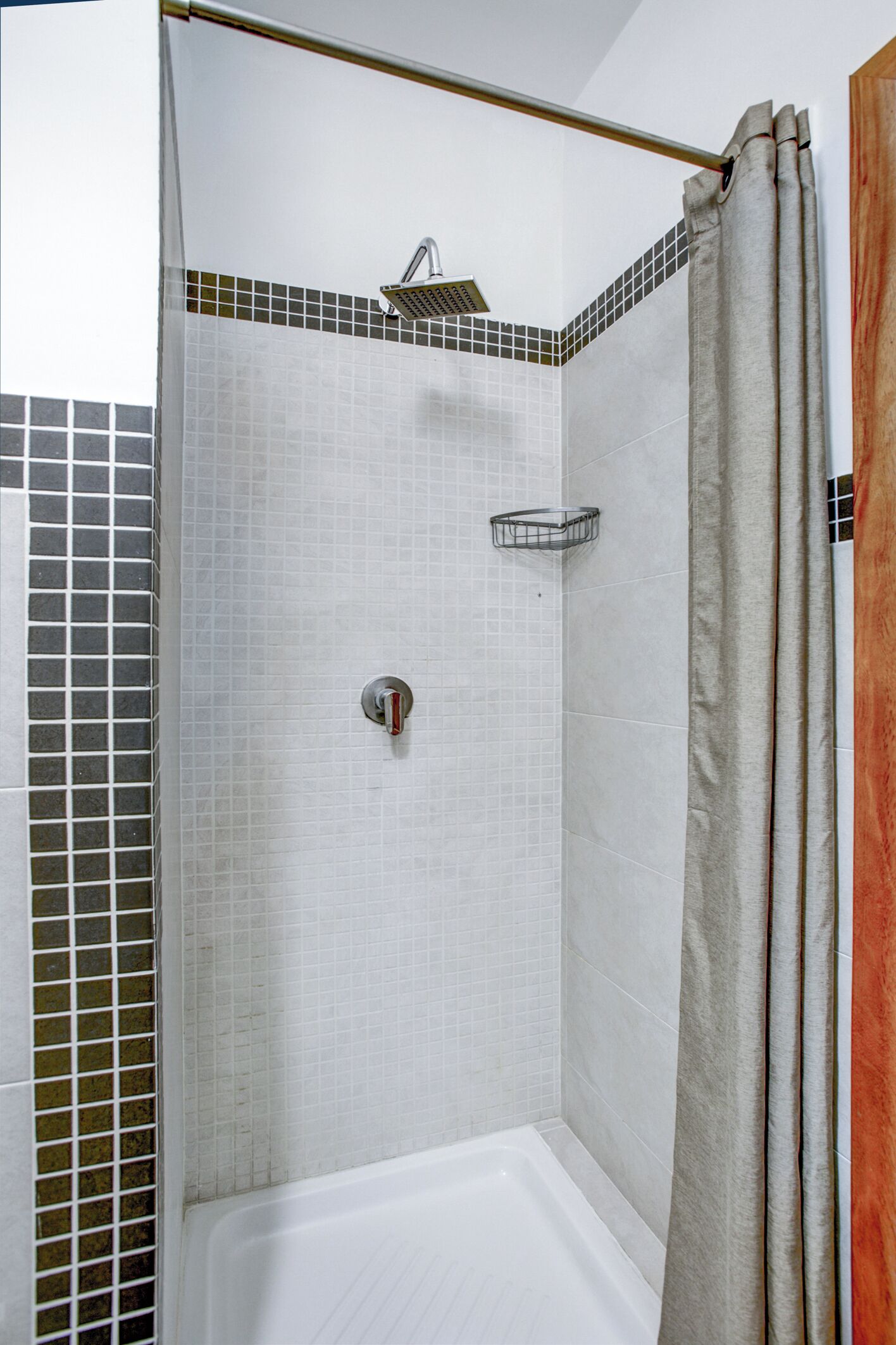 Un espace douche avec un mur carrelé, un pommeau de douche fixe, un pommeau de douche à main et un porte-savon.