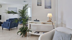 Un salon moderne avec une console blanche, un canapé bleu, un fauteuil blanc et une grande plante verte.