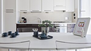 Une cuisine moderne avec des meubles blancs, une machine à café et une petite plante en pot posée sur le plan de travail.