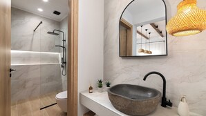 A modern bathroom with a large, round vessel sink, a freestanding mirror, and a shower area.