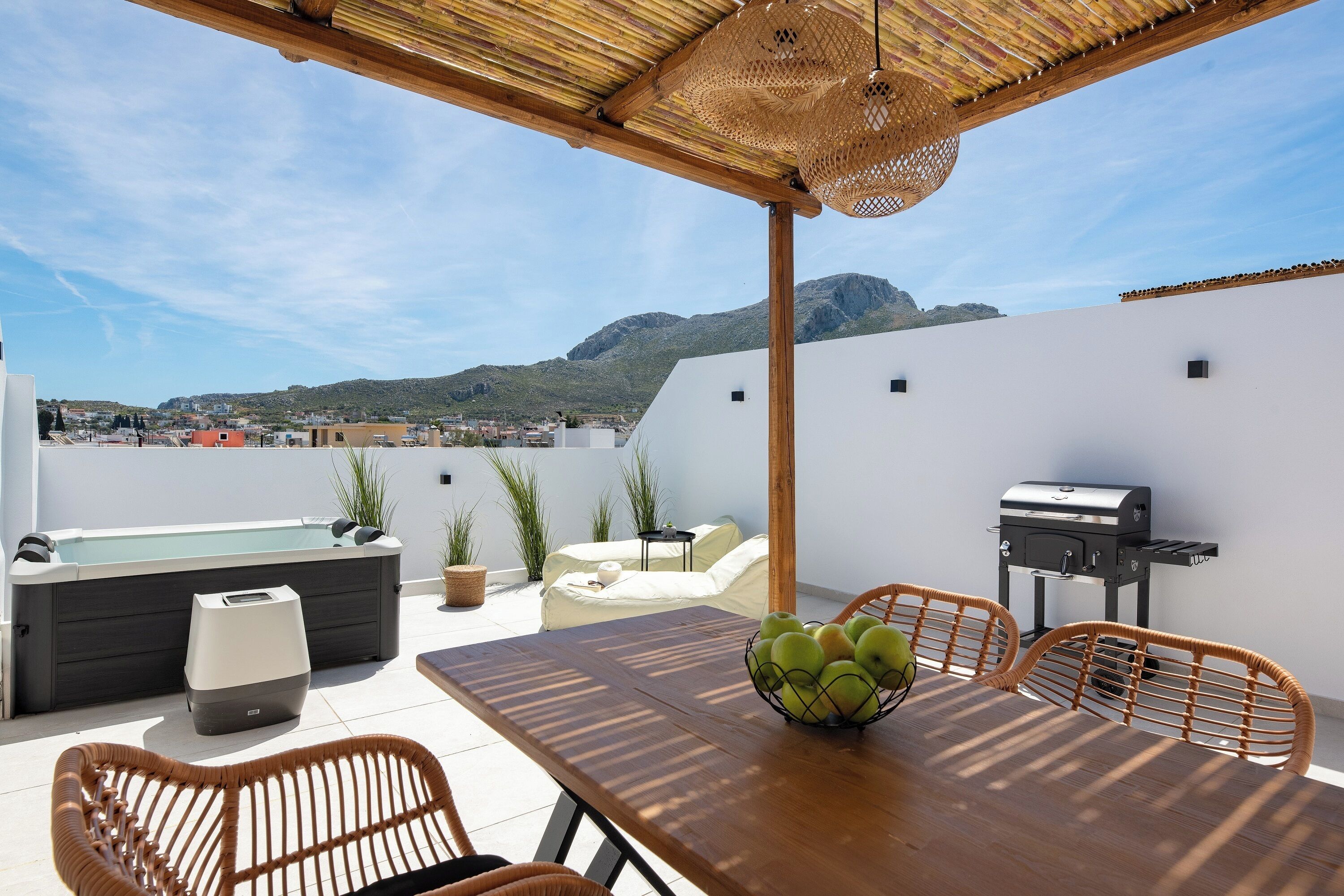 Une terrasse sur le toit avec une table en bois, des chaises en osier, un barbecue et un jacuzzi.