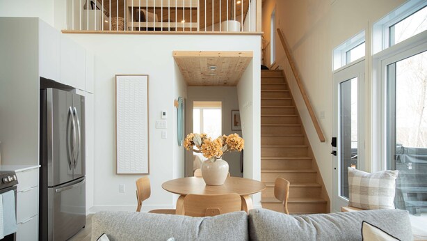 A modern kitchen with a stainless steel refrigerator, a dining area with a round table and chairs, and a staircase leading to an upper level.